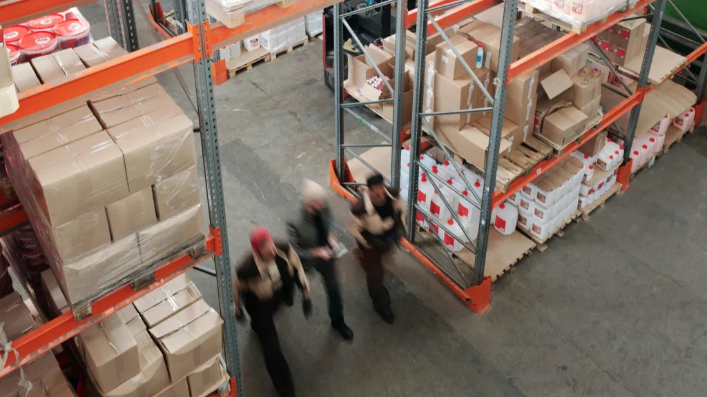 Warehouse workers inspecting supply chain inventory in a distribution centre with stacked pallets and boxes