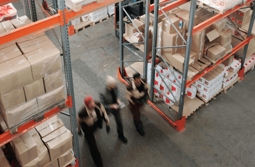 Warehouse workers inspecting supply chain inventory in a distribution centre with stacked pallets and boxes