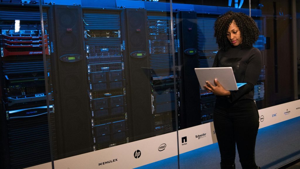 An IT professional managing server racks using a laptop, representing the integration of autonomous digital labour and corporate data governance in the SaaS revolution.