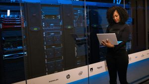 An IT professional managing server racks using a laptop, representing the integration of autonomous digital labour and corporate data governance in the SaaS revolution.