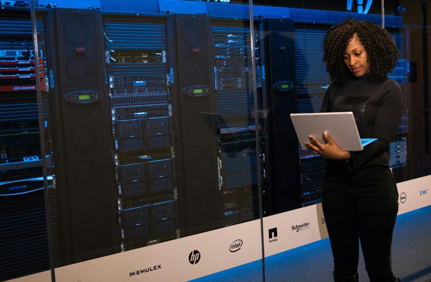 An IT professional managing server racks using a laptop, representing the integration of autonomous digital labour and corporate data governance in the SaaS revolution.