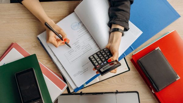 A business founder sitting at a desk, using a calculator and pen to review financial documents, cash flow, and operational costs.