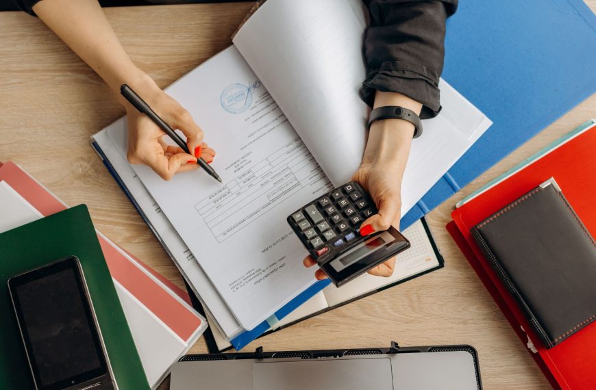 A business founder sitting at a desk, using a calculator and pen to review financial documents, cash flow, and operational costs.