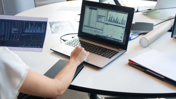 A business professional reviewing financial data and performance metrics on a laptop dashboard and printed charts.