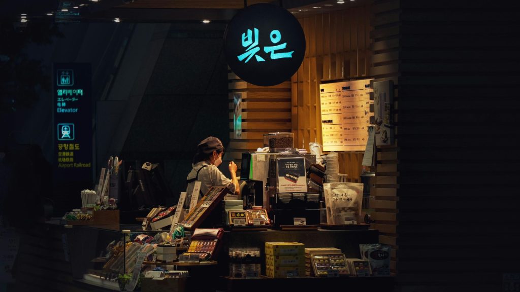 A person working at a small, illuminated retail kiosk in a transit hub, representing the agility of modern micro-multinationals.