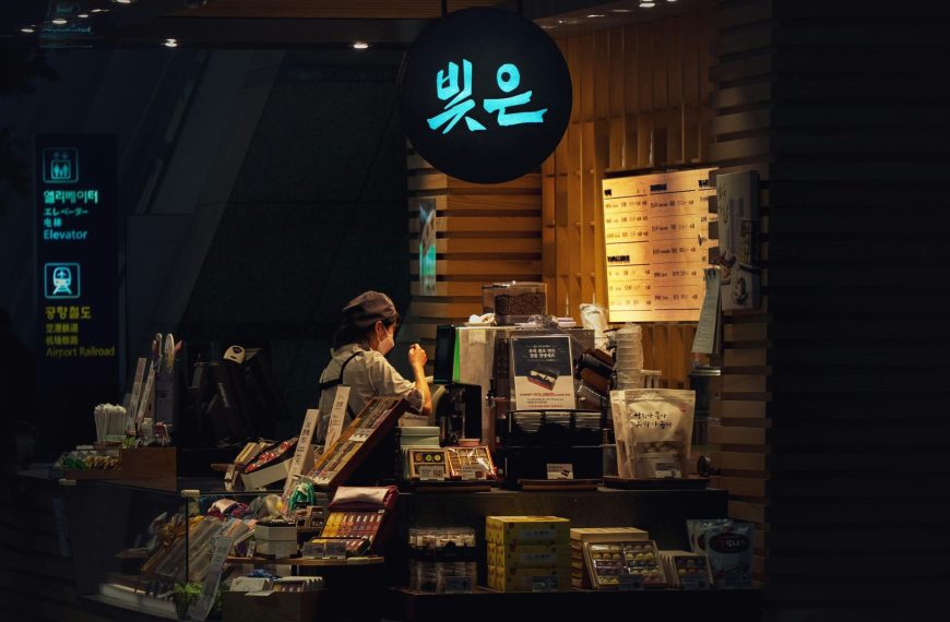 A person working at a small, illuminated retail kiosk in a transit hub, representing the agility of modern micro-multinationals.