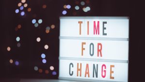 A brightly lit cinematic lightbox displaying the phrase "TIME FOR CHANGE" against a dark background with bokeh lights.