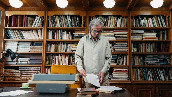 An experienced consultant standing at a wooden desk in a classic library, reviewing strategic documents next to a typewriter, illustrating the value of market research and commercial intelligence.