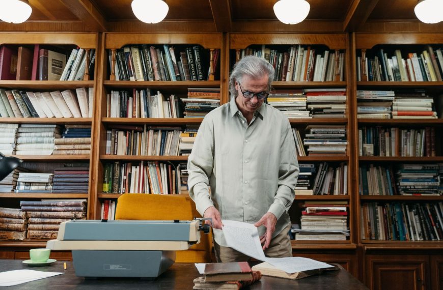 An experienced consultant standing at a wooden desk in a classic library, reviewing strategic documents next to a typewriter, illustrating the value of market research and commercial intelligence.