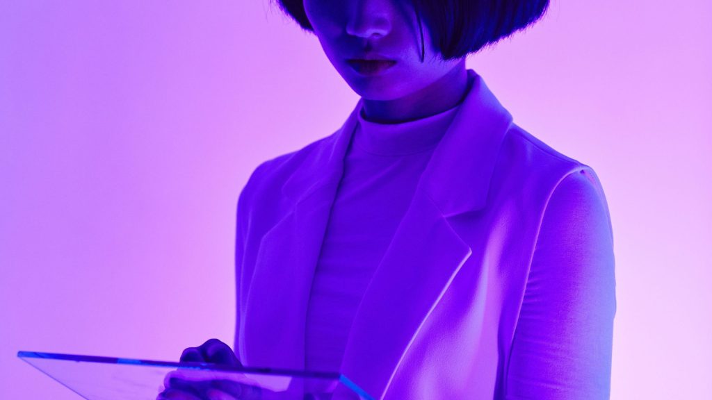 A woman in a white blazer illuminated by vibrant purple light, reviewing data on a transparent tablet, representing the data-driven approach of femtech innovation.