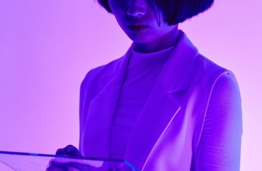 A woman in a white blazer illuminated by vibrant purple light, reviewing data on a transparent tablet, representing the data-driven approach of femtech innovation.
